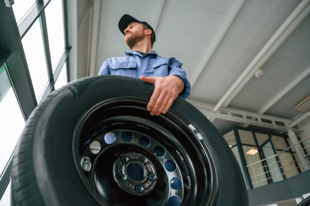 A tire service worker with a big, new tire, preparing for tire replacement.