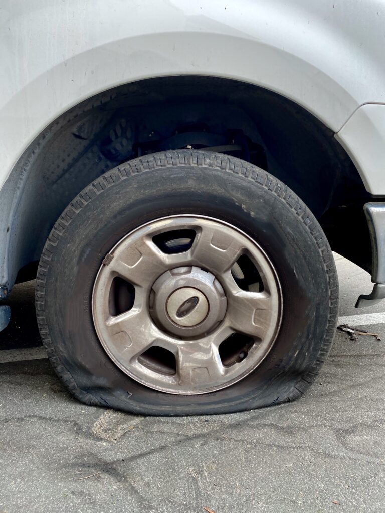 Damaged tire after a tire blowout, resting flat on the ground.